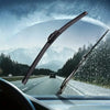Close-up view of a car windshield with water droplets, showing universal wiper blades in use on an open road.