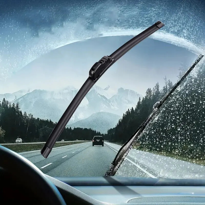 Close-up view of a car windshield with water droplets, showing universal wiper blades in use on an open road.