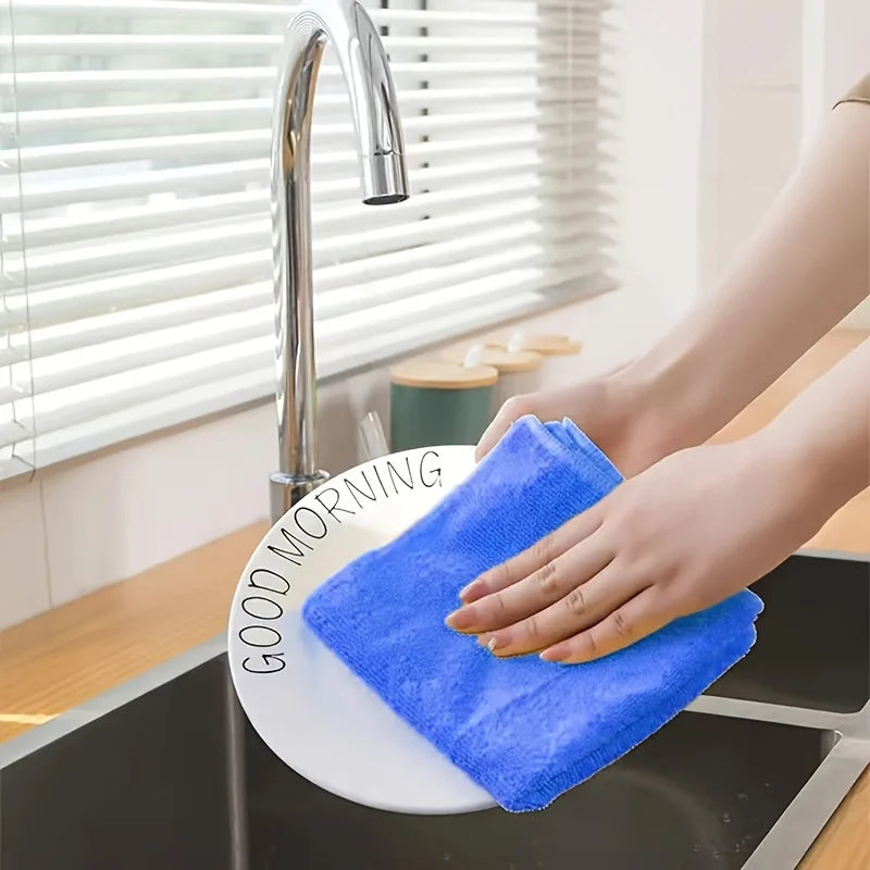 A hand is using a blue microfiber cloth to clean a kitchen sink under a faucet.