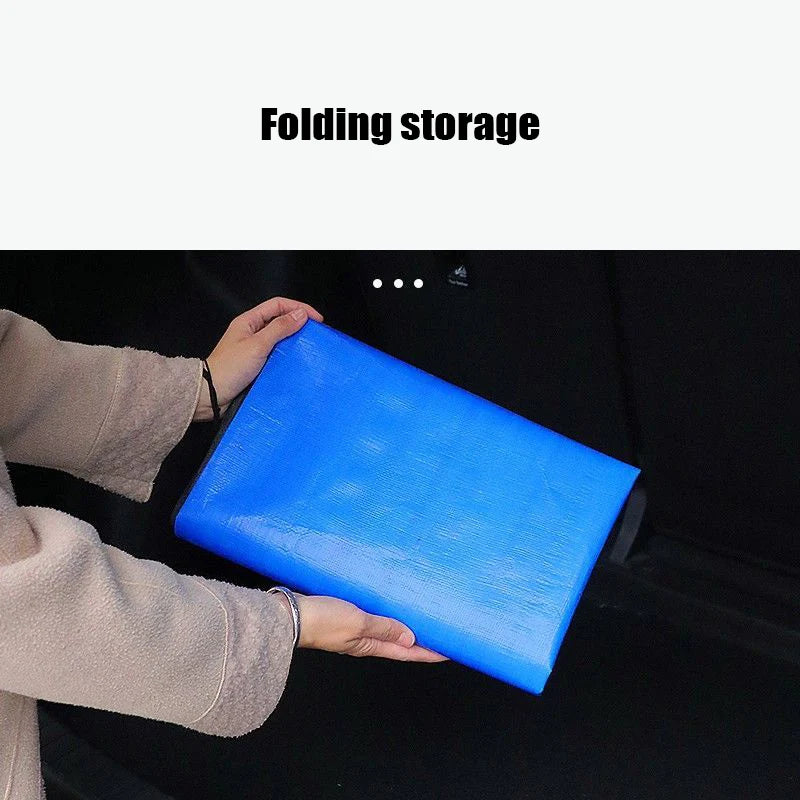 A hand is holding a bright blue folding storage mat designed for car trunk lining.