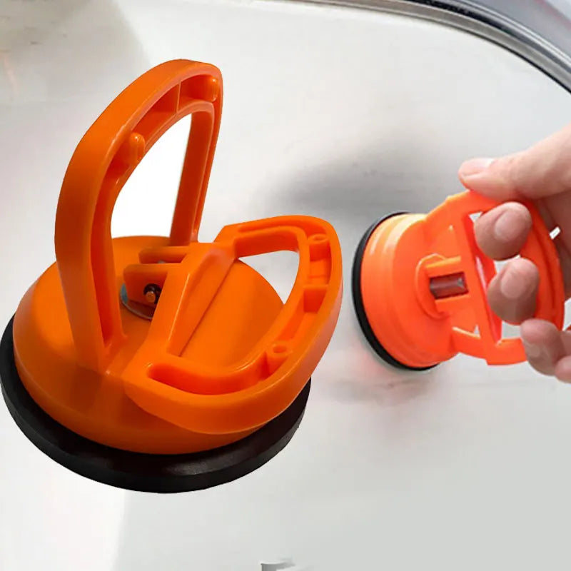 An orange car dent remover puller with a suction cup is held by a hand.