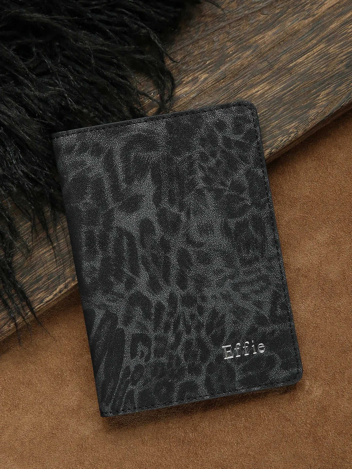 A black leopard print passport holder resting on a brown surface next to dark fur.