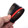 A black carbon fiber rearview mirror rain shield is held in a hand, showing its dark tint and red accent ring.