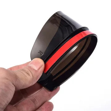 A black carbon fiber rearview mirror rain shield is held in a hand, showing its dark tint and red accent ring.