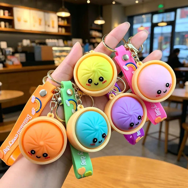 A hand holds several cute silicone keychains shaped like bao buns in various pastel colors and designs.