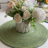Composition florale de roses blanches et d'herbes séchées sur un sous-plat rond en tissé vert.