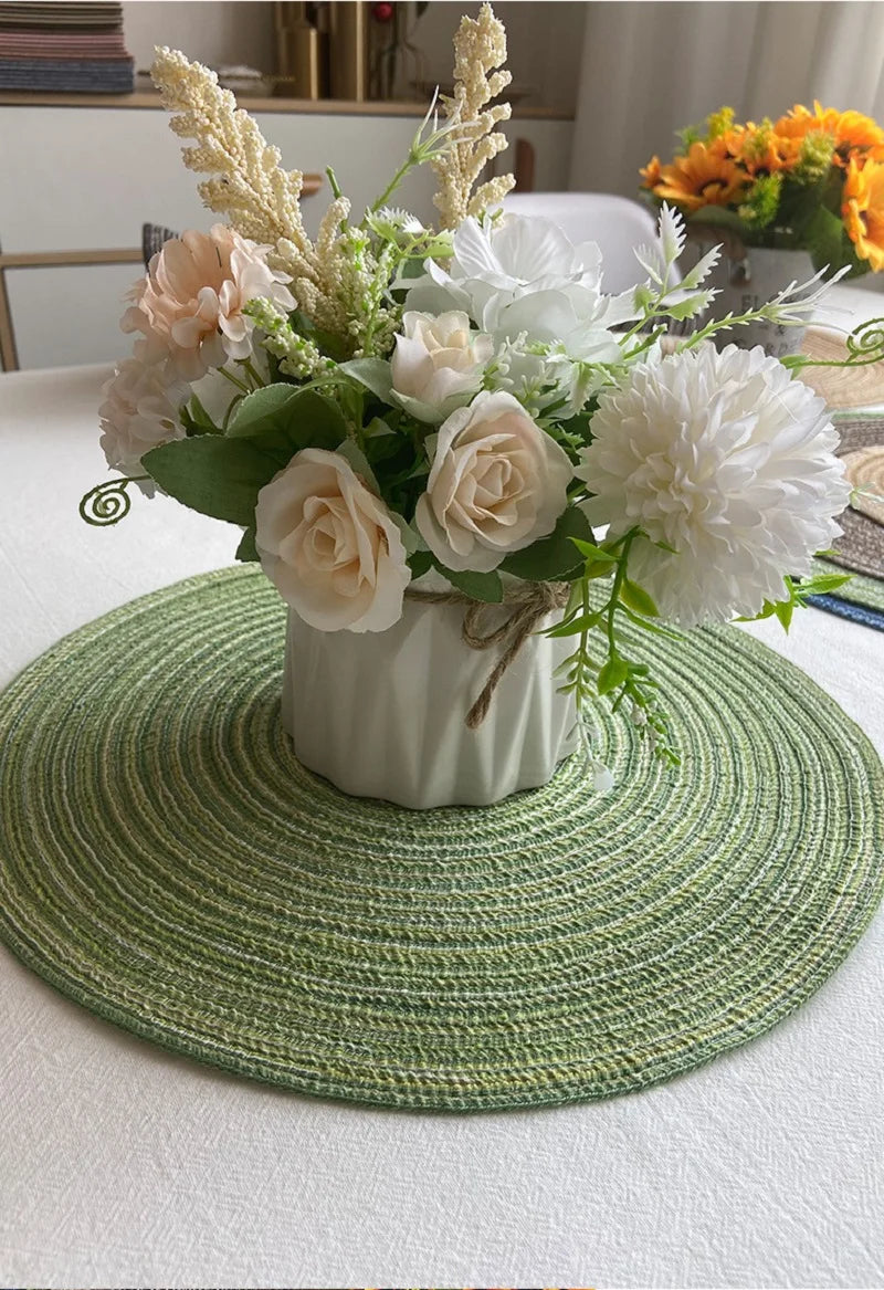 Composition florale de roses blanches et d'herbes séchées sur un sous-plat rond en tissé vert.