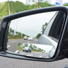 A close-up view of a black 360 degree convex angle car mirror reflecting the road and surrounding scenery.