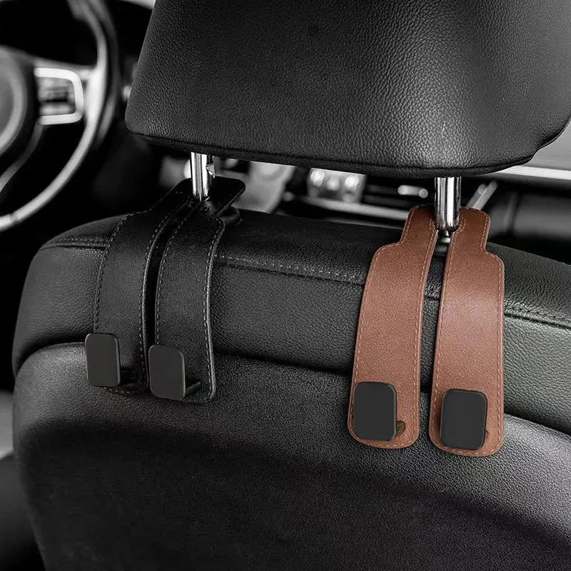 Car headrest hooks in brown leather attach to a black car seat for bag organization.