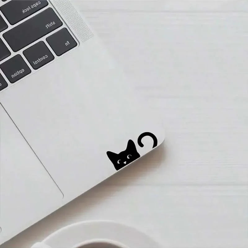 A white laptop with a black cat decal on the lid, placed next to a white cup.