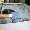 A hand wearing a white glove is cleaning a car's windshield with a blue microfiber detailing glove.