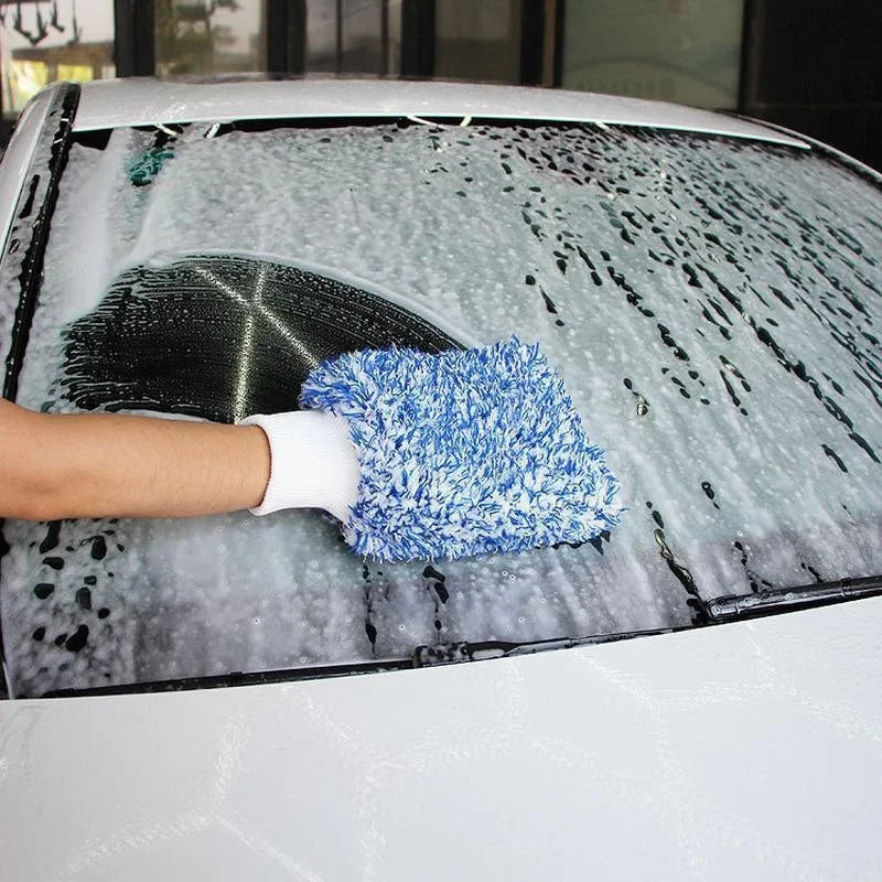 A hand wearing a white glove is cleaning a car's windshield with a blue microfiber detailing glove.
