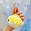 A yellow plush bunny with white accents is being held by a hand, attached to a gold ring keychain.