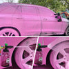 A close-up of a pink car being cleaned with a high-pressure foam lance on the wheel.