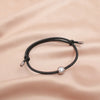 A black fitness tracker bracelet with a silver charm is displayed on a smooth, light pink fabric.