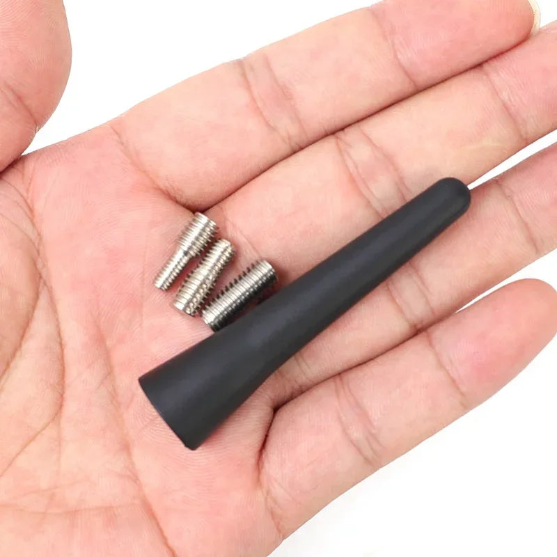 A hand holds a black universal car roof antenna with several mounting screws.