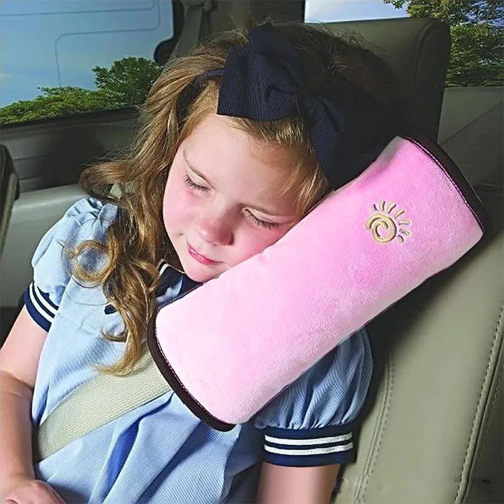 A young girl rests her head on a pink shoulder cushion designed as a universal car seat belt for kids.
