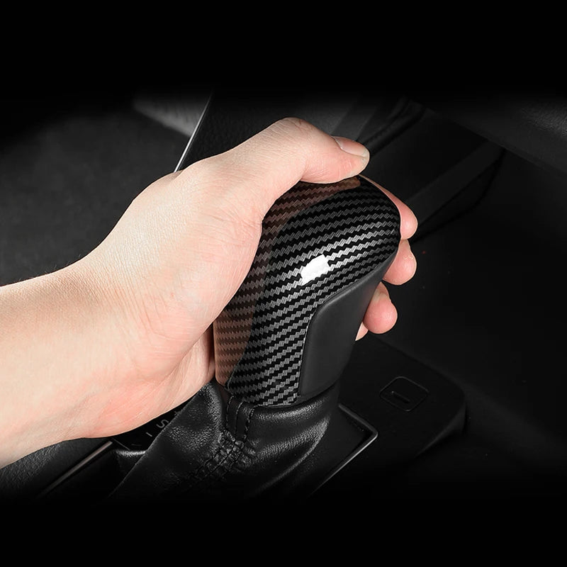 Eine Hand greift die Abdeckung des Carbonfaser-Schaltknaufs in der Fahrzeugkonsole.