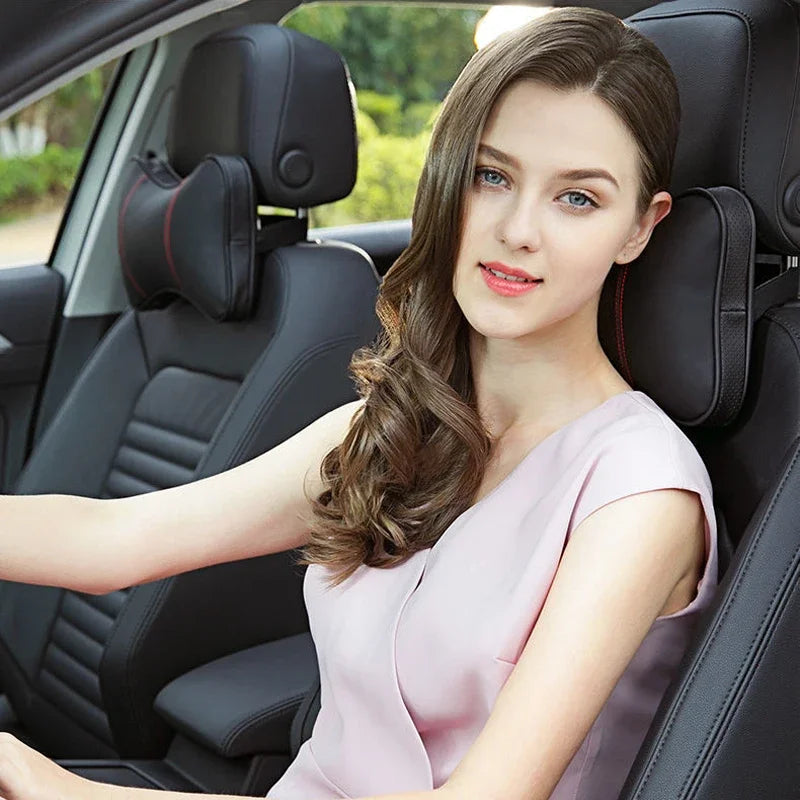 A young woman sits in a car seat, wearing a light pink top, with the headrest and seatbelt pads visible.