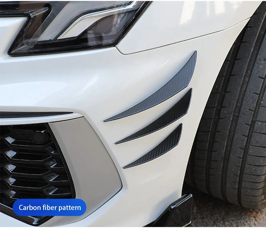 Close-up of a white car bumper featuring black carbon fiber pattern spoiler fins.