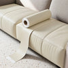 A roll of beige self-adhesive PU leather repair patches resting on a light-colored upholstered surface.