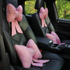 Pink bowknot car neck pillows resting on the seats of a black vehicle interior.