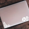 Ein weißes Laptop mit zarten weißen Hibiskusblüten-Aufklebern auf dem Deckel, auf einer Holzoberfläche.