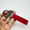 A red suede leather keychain with a silver split ring attached to a metal fob is held in a hand.