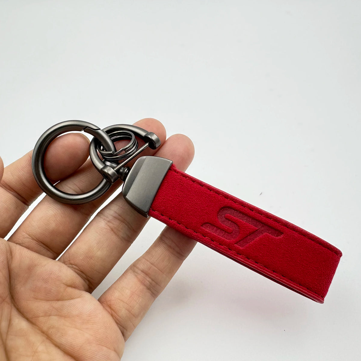 A red suede leather keychain with a silver split ring attached to a metal fob is held in a hand.