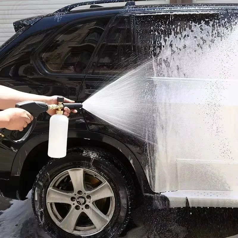 A hand is using a foam pressure washer kit to clean the exterior of a black SUV.