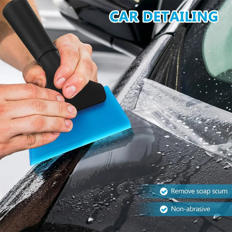 Hands using a blue squeegee tool to remove soap scum from a car window during car detailing.