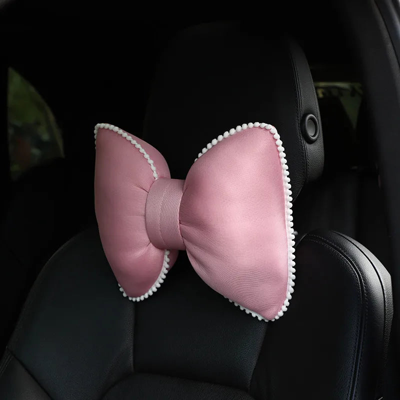 Pink ergonomic car headrest pillow with a bow design placed in a black car seat.