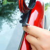 A hand is applying a black sealing strip to the edge of a red car window or roof.