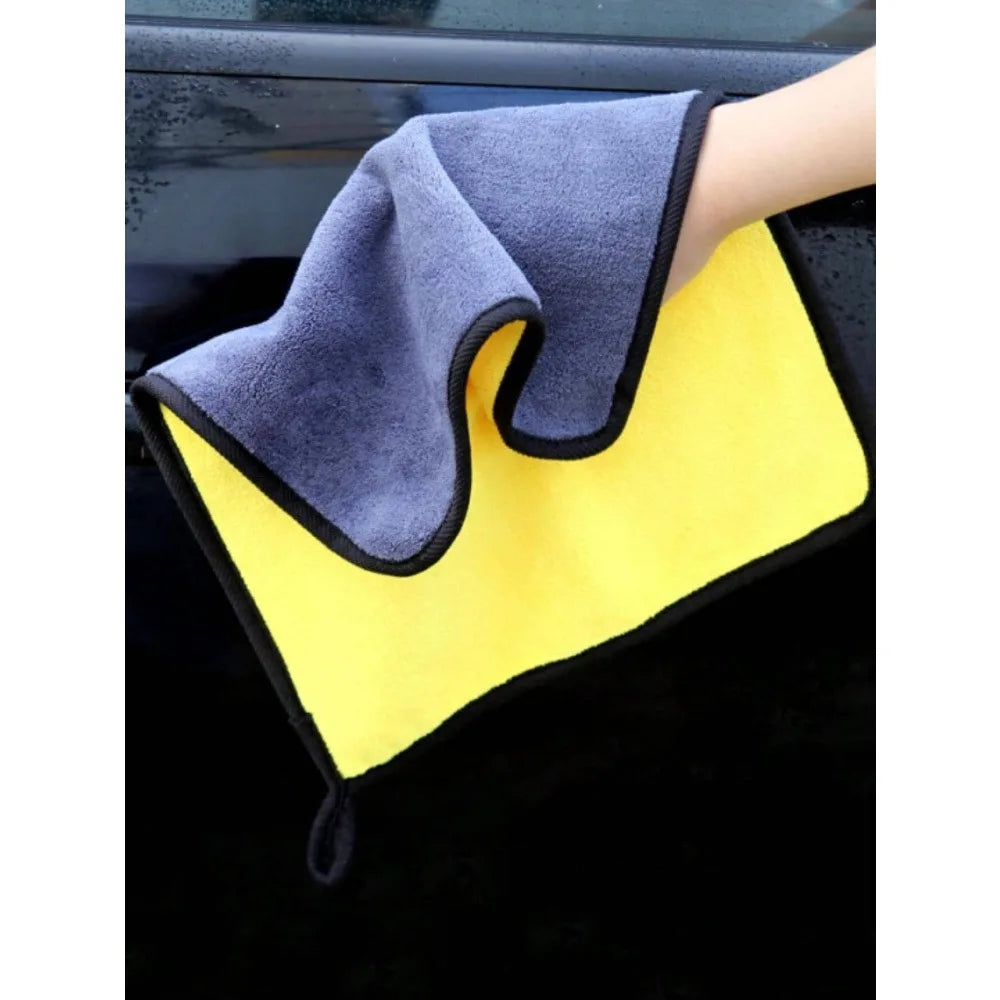 A hand is holding a dark gray microfiber car cleaning towel resting on a bright yellow towel.