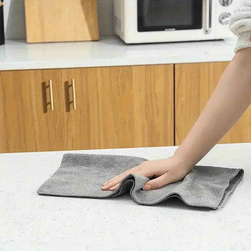Eine Hand legt ein graues Mikrofasertuch auf eine weiße Arbeitsplatte in einer Küche.