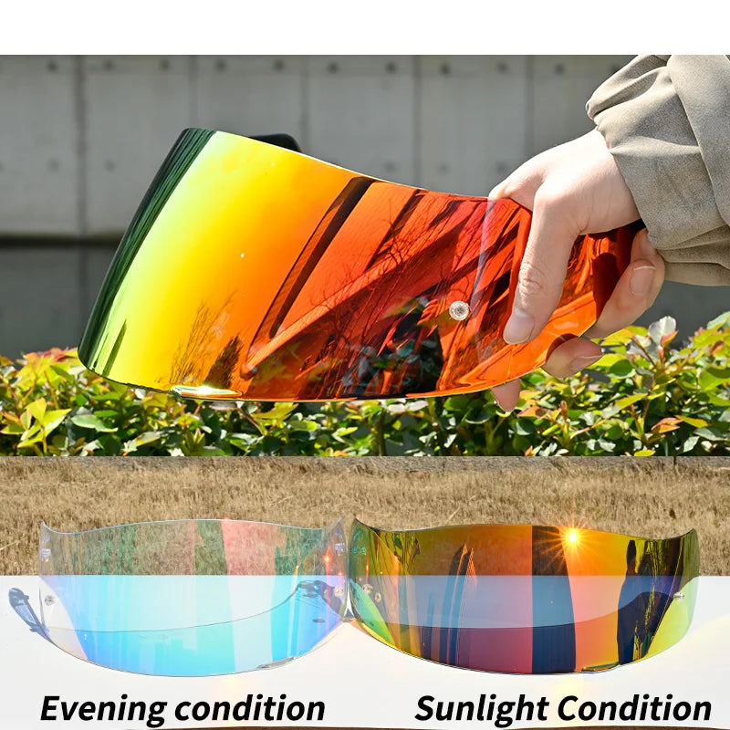 A hand holds a tinted motorcycle helmet visor showing sunset colors in evening and sunlight conditions.