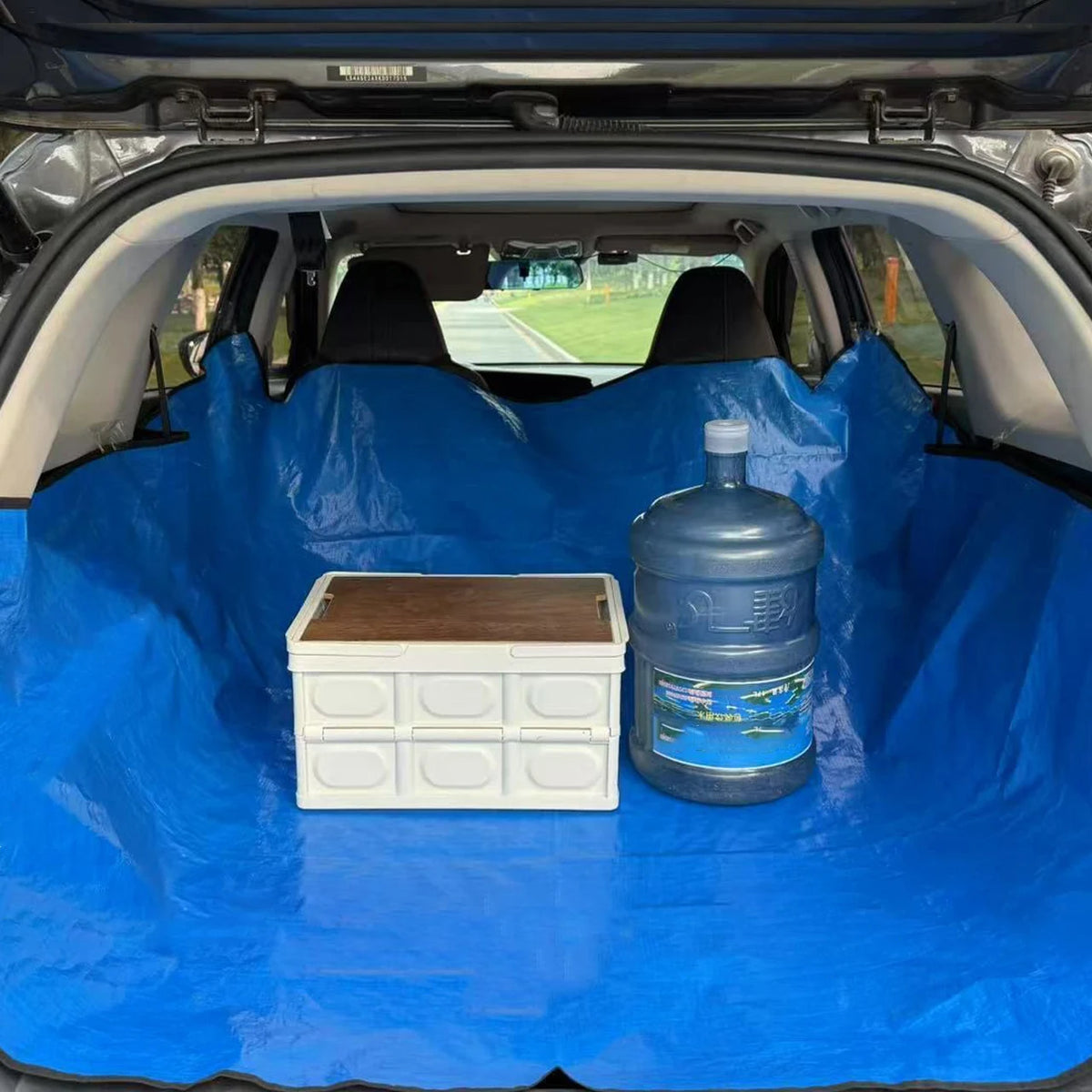 A blue car trunk liner mat with a white storage box and a plastic bottle inside.