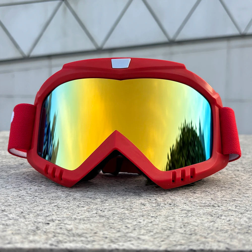 A red windproof sports goggle with a yellow-tinted lens resting on a gray surface.