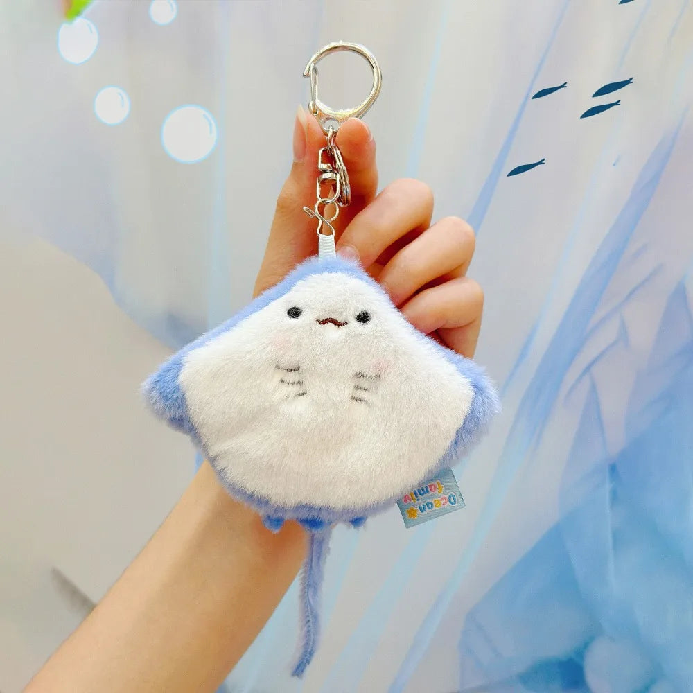 A hand holds a small, light blue plush bunny keychain with soft fur and a gold ring against a light blue background.