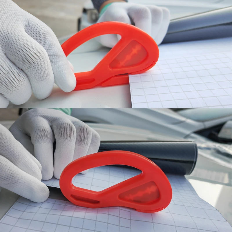 A hand wearing a white glove is using an orange professional car vinyl wrapping tool on a sheet of paper.