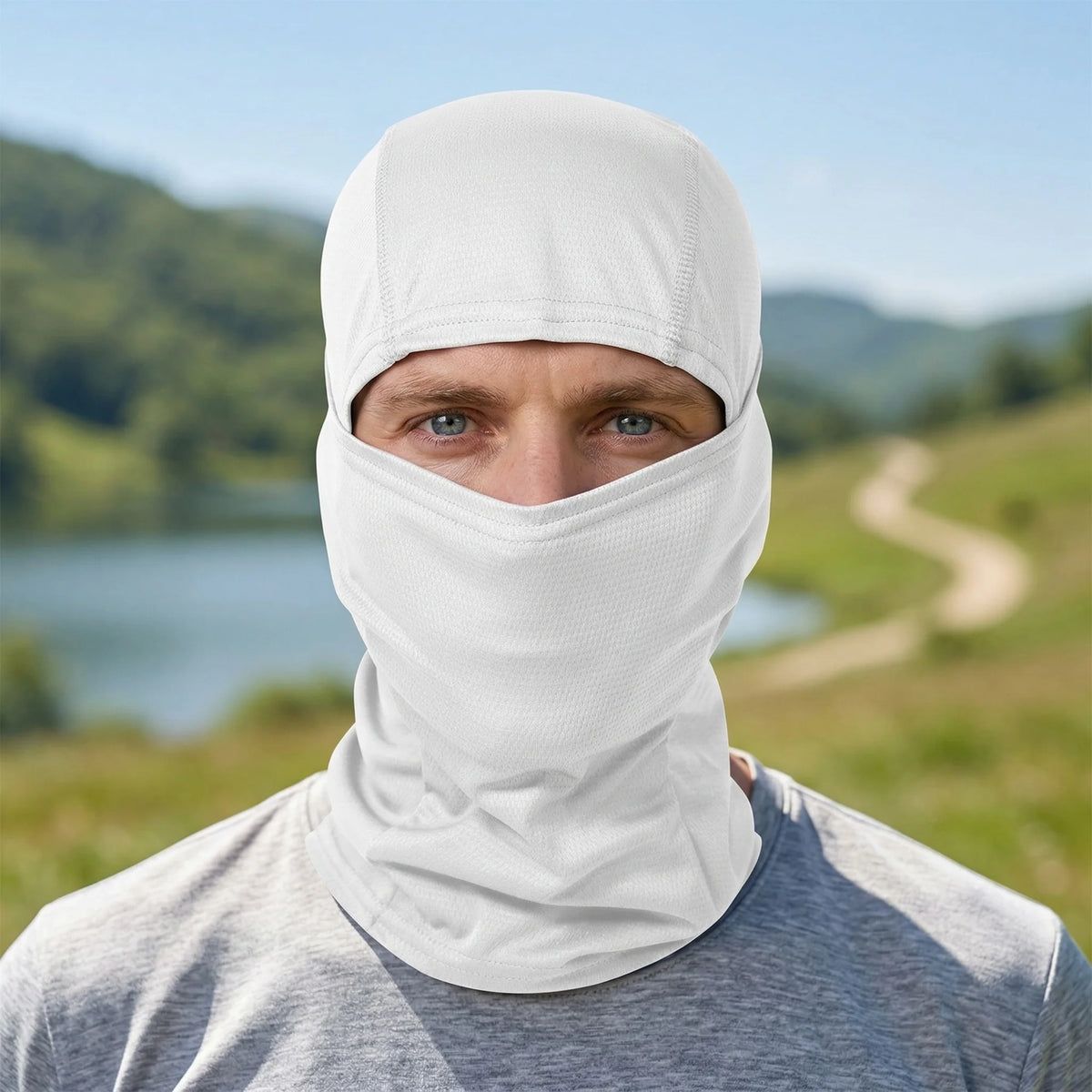 A man wearing a white multi-functional stretchy balaclava cap for outdoor sports against a scenic, green landscape.
