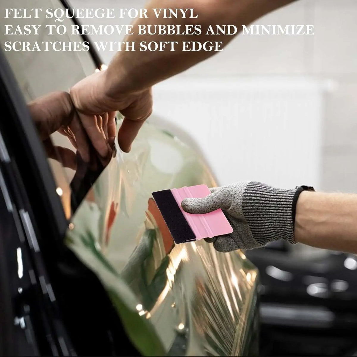 A hand uses a felt squeegee tool to remove bubbles and scratches from a clear vinyl film.