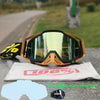 A pair of orange and black motocross goggles resting on a white cloth with a lens insert.