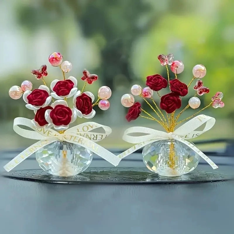 A crystal rose dashboard ornament featuring red and pink faux roses with pearl accents tied with a white ribbon.
