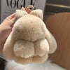 A light beige plush bunny keychain with soft fur and a gold ring being held by a hand.