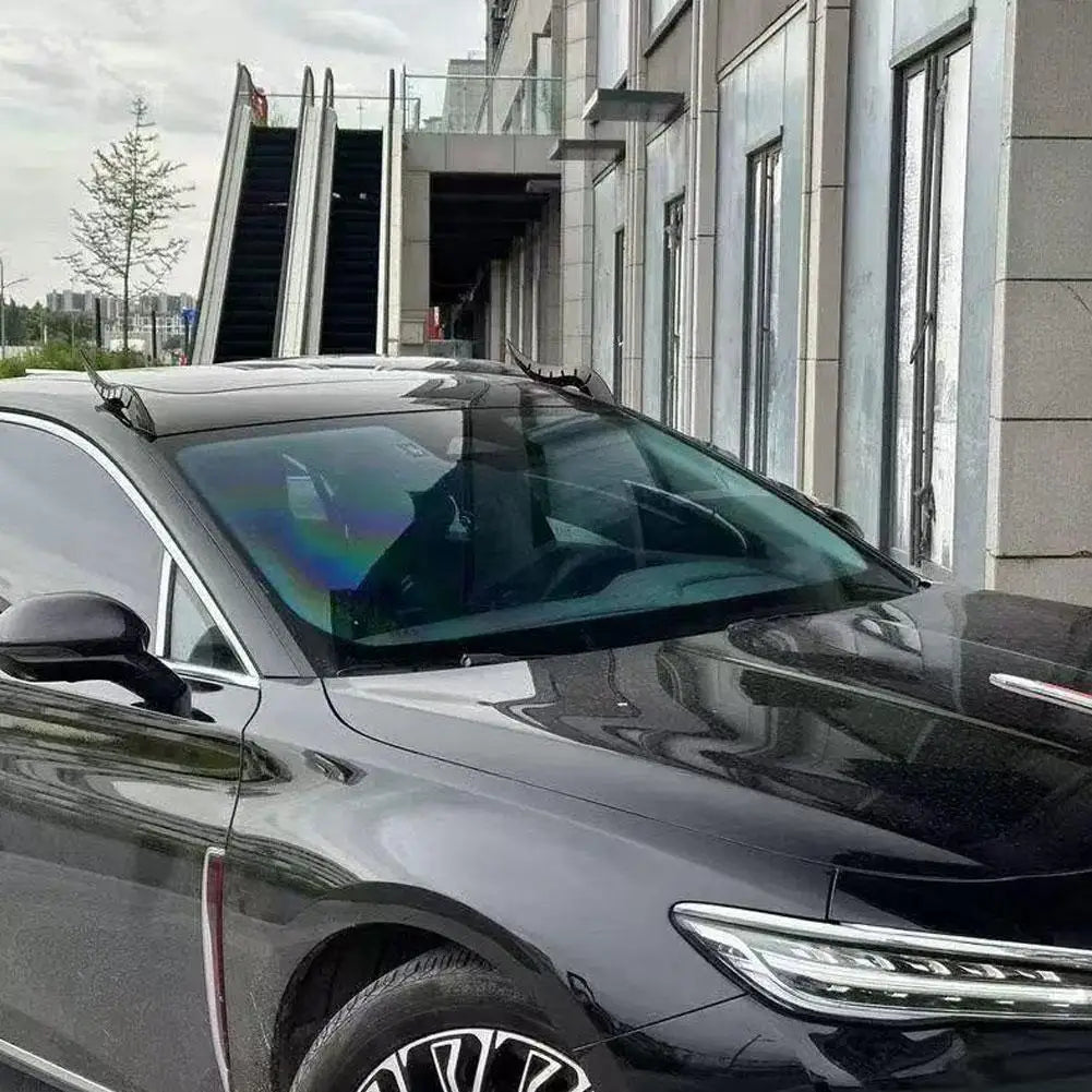 A black car with a dragon horn roof decor accessory parked in front of a modern building.