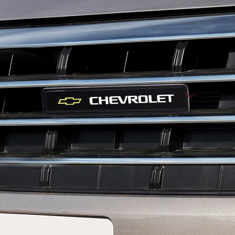 Close-up of a black car grille featuring the Chevrolet logo and an LED light.