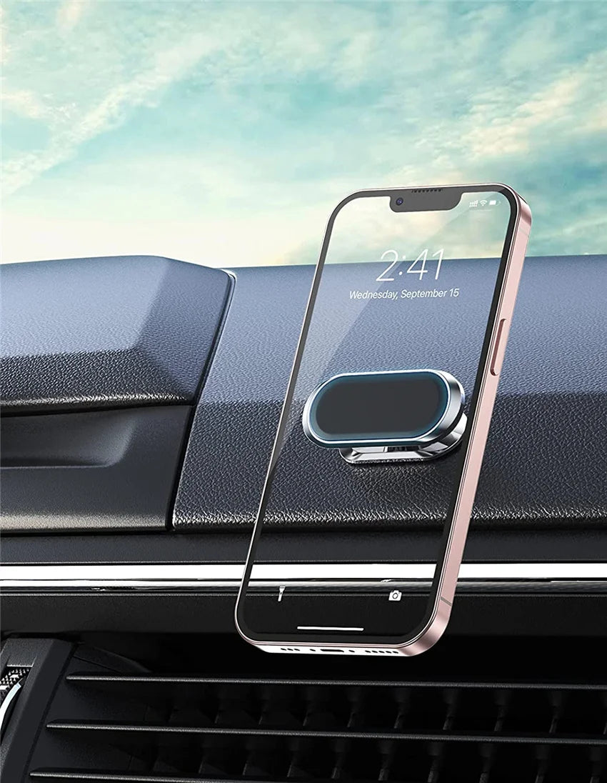 A pink iPhone is mounted in a magnetic car phone holder on a dark car dashboard.