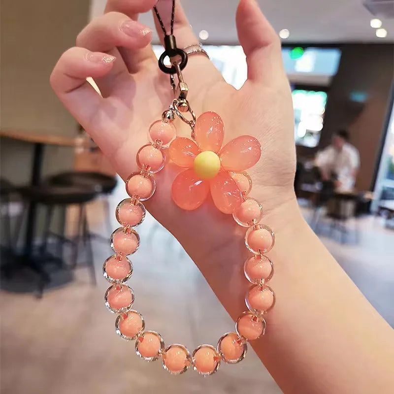 A hand holds a phone anti-loss lanyard featuring a round bead pendant with an orange flower design.