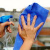 A hand is wiping a window with a blue microfiber cleaning cloth while a spray bottle is visible.
